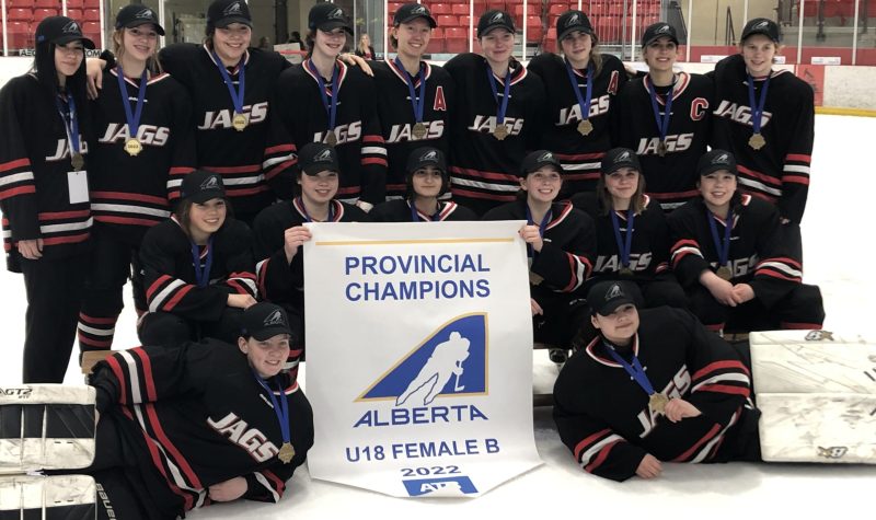 The 2022 U18 Provincial Champions Lakeland Jaguars posing in front of their championship banner at center ice.