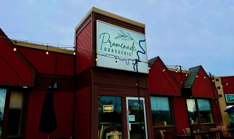 Le restaurant Promenade Brasserie écrit sur une enseigne en vert. Le bâtiment est de couleur rouge et le ciel est nuageux.
