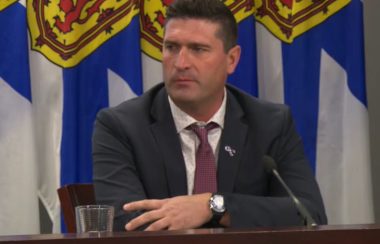 Geoff MacLellan un homme entre 40 et 50 ans en conférence de presse devant les drapeaux néo écossais, il est tourné vers la droite