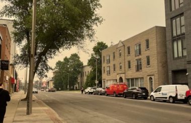 Princess Street in Kingston, Ontario on Tuesday June 6. The bottom portion of the image captures the street and a few buildings. The sky in the upper third of the image is completely obscured by yellow-ish smoke.The image appears to have a yellow, cloudy filter over it due to the wildfire smoke.