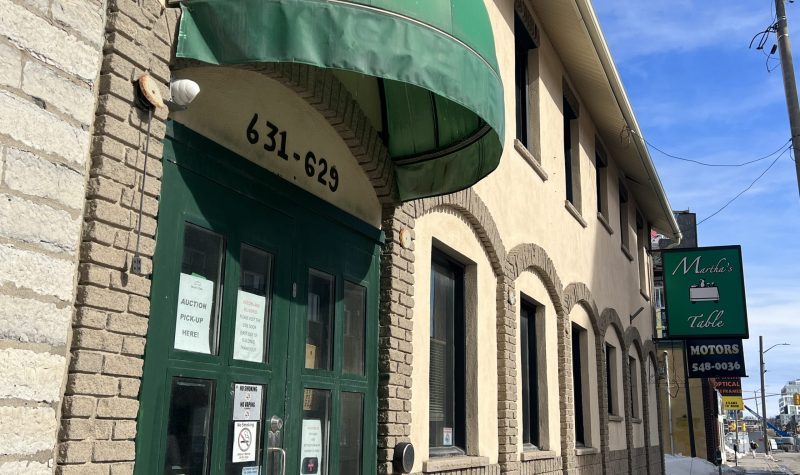 An old beige building is pictured from the side angle. A green half moon roof is over green doors that opens to Martha's Table. The Martha's Table sign is on the further right side of the building.