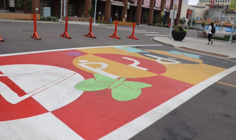A colorful crosswalk on Okîsikow (Angel) Way in Edmonton, showing Indigenous language and arts. Weather is cloudy.