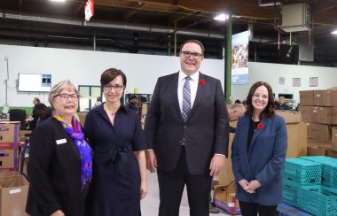 A group of three women and one man stand together inside of the Edmonton Food Bank for a photo.