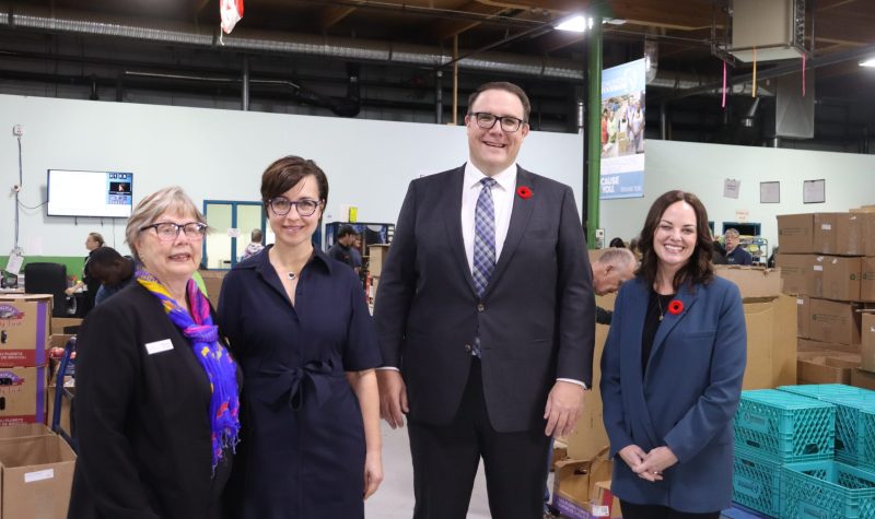 A group of three women and one man stand together inside of the Edmonton Food Bank for a photo.