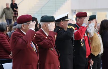 Métis veterans salute during the playing of the Métis national anthem. They are all in unique uniforms and wearing medals.
