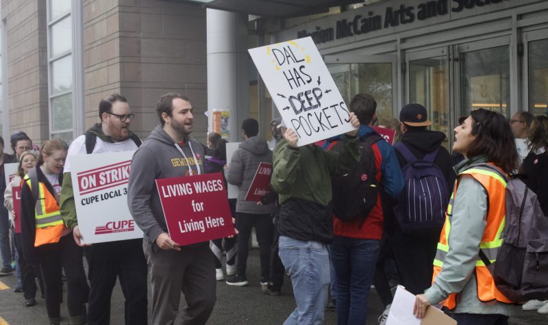 A CUPE 3912 union members forming a picketing line in front of Dalhousie's building. Men and women are seen holding posters asking for wage increases.