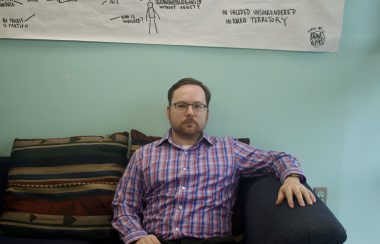 A man sitting on a couch and looking at the camera. He is in CKDU's station.