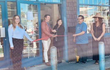 Four people outside a local business doing a ribbon cutting