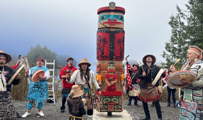 drumming singing and cultural dancing outside around a 10 foot totem pole.