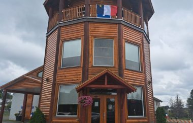 Tour des Pionniers en bois brun affichant un drapeau de l'Acadie en hauteur, lors d'une pluvieuse et nuageuse