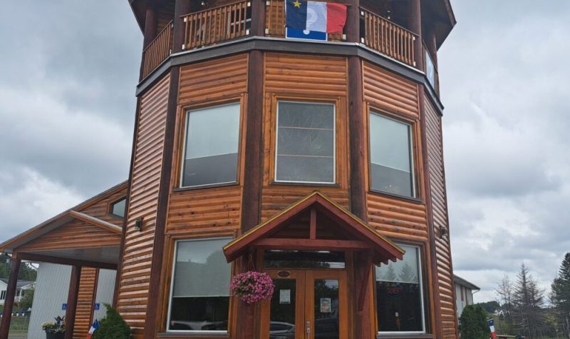 Tour des Pionniers en bois brun affichant un drapeau de l'Acadie en hauteur, lors d'une pluvieuse et nuageuse