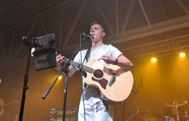 Homme vêtu de blanc tenant une guitare et chantant lors d'un concert
