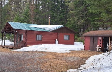 Chalet de couleur rouge entouré de conifères avec quelques butes de neige. lors d'une journée de printemps.