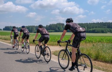 Quatre cyclistes portant le même habit roule sur l'accotement d'une route, lors d'une belle journée ensoleillé avec quelques nuages