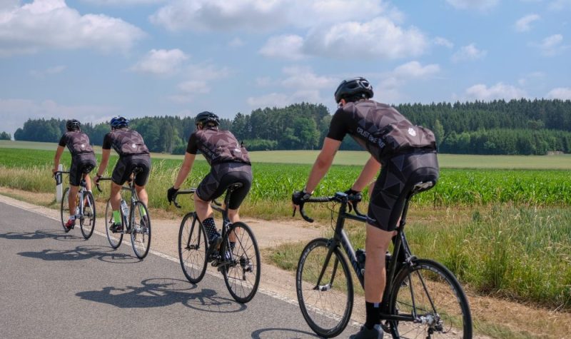 Quatre cyclistes portant le même habit roule sur l'accotement d'une route, lors d'une belle journée ensoleillé avec quelques nuages