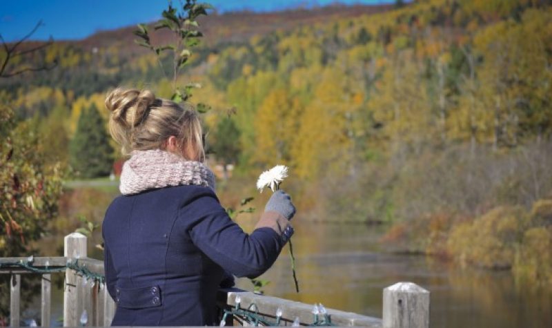 Femme qui a une fleur à la main, devant un lac.