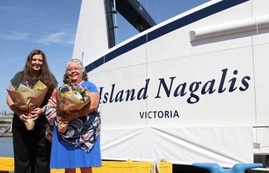 Two smiling women stand holding bouquets in front of newly christened BC Ferry