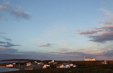 Un ciel bleu au-dessus d'une vingtaine de maisons regroupées sur une île. Parmi-celles-ci, on remarque une chapelle.