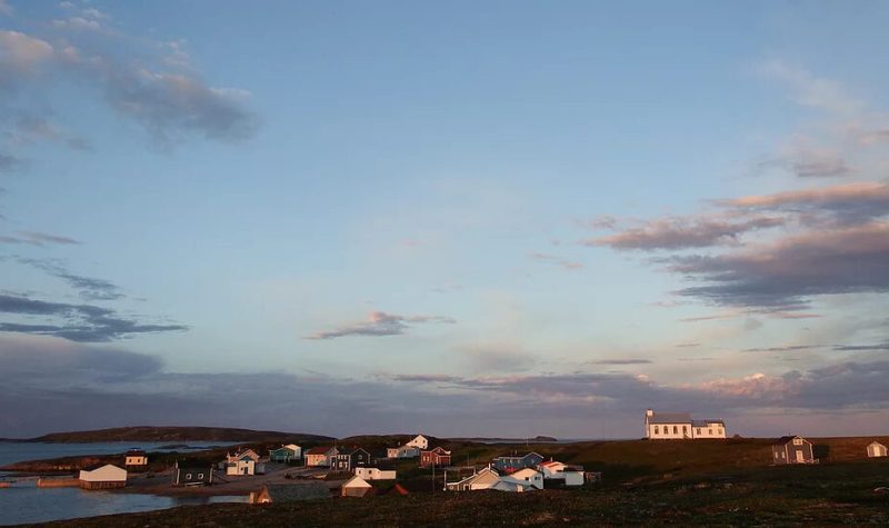 Un ciel bleu au-dessus d'une vingtaine de maisons regroupées sur une île. Parmi-celles-ci, on remarque une chapelle.