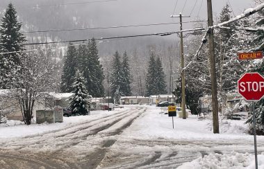 A stop sign with the street name, Oscar Street in the foreground, snowy intersection, mobile homes lining the street in the background.