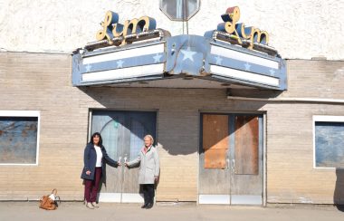 Fort-Coulonge Mayor Christine Francoeur and MRC Pontiac Warden Jane Toller stand in front of a run down theatre with a rusty marquee and plywood covering the windows and doors.