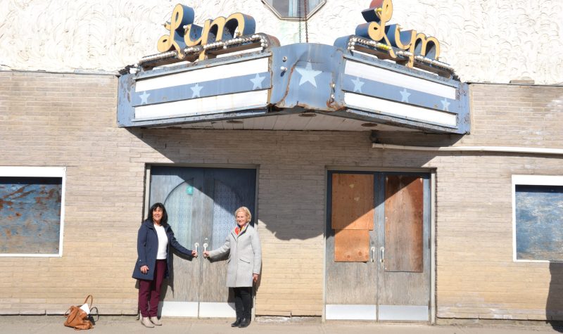 Fort-Coulonge Mayor Christine Francoeur and MRC Pontiac Warden Jane Toller stand in front of a run down theatre with a rusty marquee and plywood covering the windows and doors.