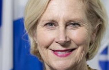 A professional headshot of Pontiac Warden Jane Toller standing in front of a Quebec flag.