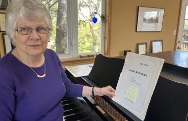 A woman wearing a purple top is shown in a sunlit room near a grand piano.