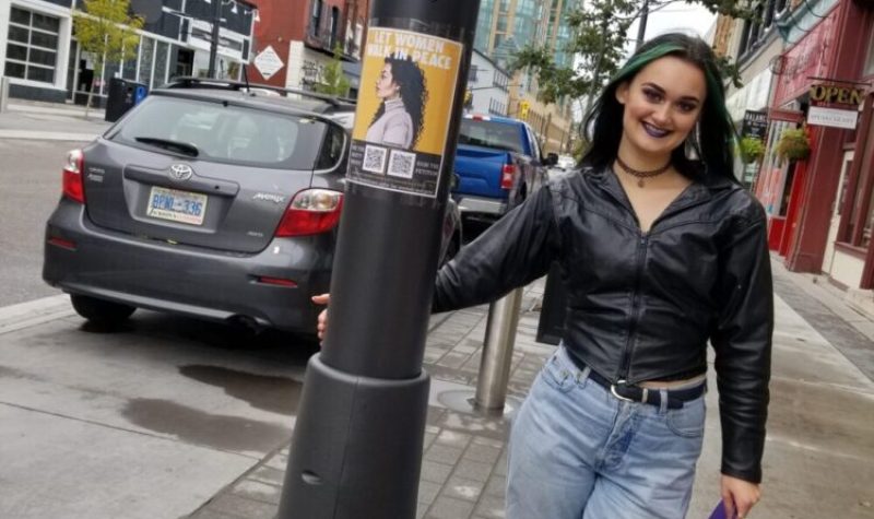 Jasmine Botter dans le centre-ville à côté dune affiche qui parle de sa pétition