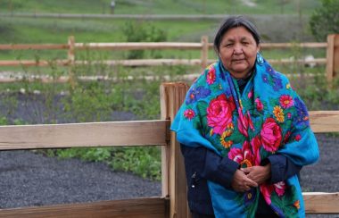 Jenette Wildman standing near the garden at the healing space garden. There is a wood fence behind her.