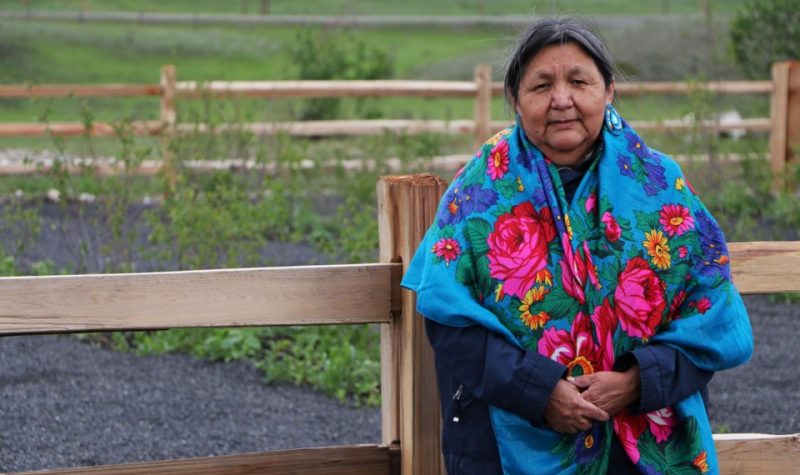 Jenette Wildman standing near the garden at the healing space garden. There is a wood fence behind her.