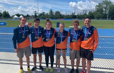 Vêtus des couleurs de la délégation de la Côte-Nord aux Jeux du Québec, six adolescents portent une ou plusieurs médailles au cou devant une piste d’athlétisme.