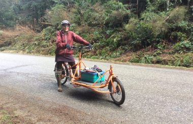 A woman riding e-cargo bike with load on rural road