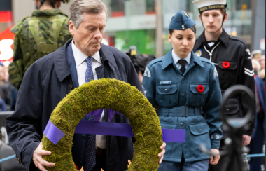 A person holds a green memoriral wreath while three people in military uniforms stand around in the background.