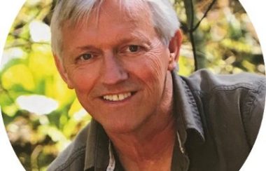 A headshot of John Vissers in front of trees/plants