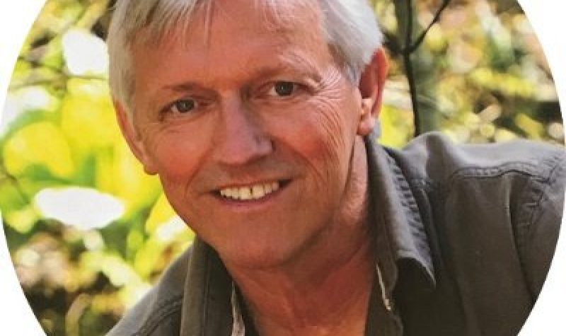 A headshot of John Vissers in front of trees/plants