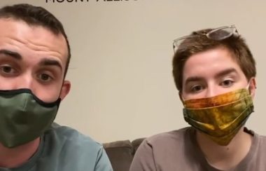 Jon Ferguson and Charlie Burke sit side-by-side on a couch with face masks on.