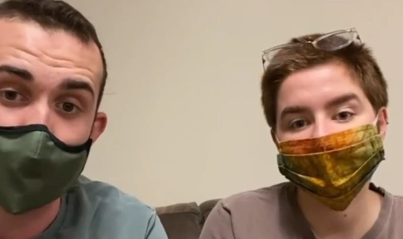 Jon Ferguson and Charlie Burke sit side-by-side on a couch with face masks on.