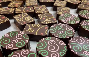 Two types of chocolates are lying on a table. One is round with green and pink swirls. The other is rectangular with yellow and red swirls.