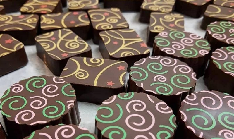 Two types of chocolates are lying on a table. One is round with green and pink swirls. The other is rectangular with yellow and red swirls.