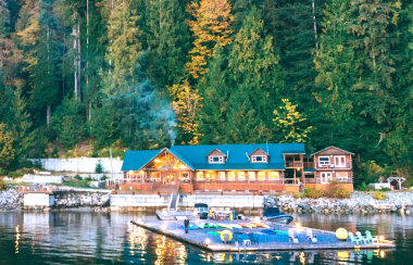 A large building at the water's edge with a square dock that has chairs and kayaks.