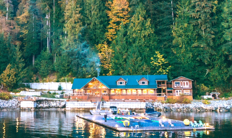 A large building at the water's edge with a square dock that has chairs and kayaks.