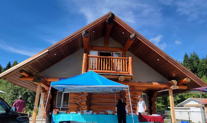 A two story log house with an angled roof and a blue tent and table at the base