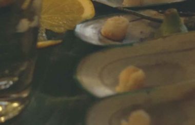 Mussel shells, a lemon wedge and a full glass on a table top.