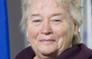 A professional headshot of Thorne Mayor Karen Daly Kelly wearing a purple sweater in front of a Quebec flag.