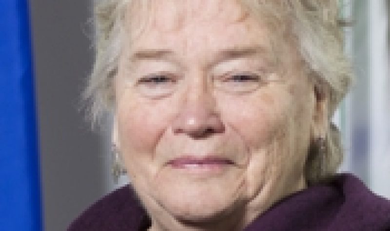 A professional headshot of Thorne Mayor Karen Kelly, wearing a purple shirt and standing in front of a Quebec flag.