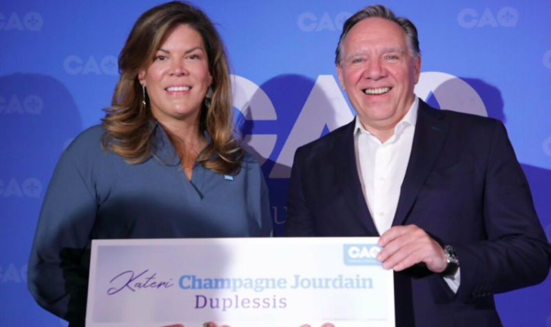 Une femme et un homme tiennent une affiche sur laquelle on peut lire Kateri Champagne Jourdain, Duplessis et le logo de la CAQ.