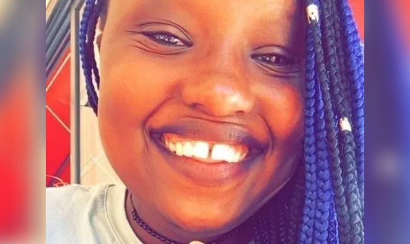 A close-up shot of a young woman's smiling broadly. She has blue and black braided hair and is wearing a light coloured shirt.