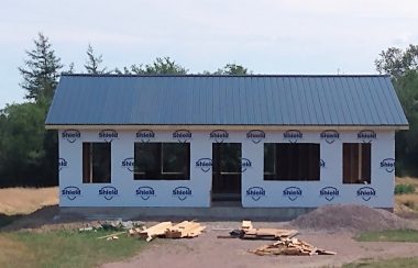 A partially built building with no windows or doors put in and construction equipment scattered in front of it.