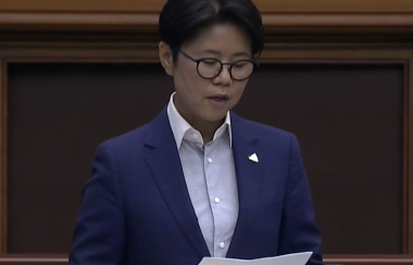 A person in a blue suit and white dress shirt. They are wearing glasses as they read a white paper.